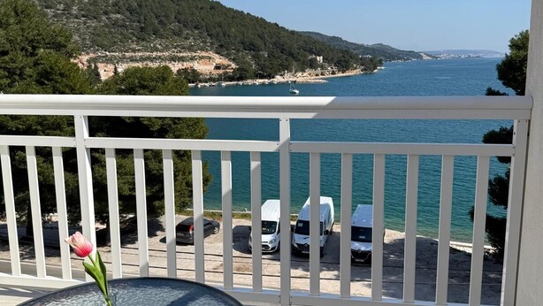 A balcony with a glass table and chairs, overlooking a body of water and a hilly landscape. - Adrian's Beach House by Max Gastro (Marina)