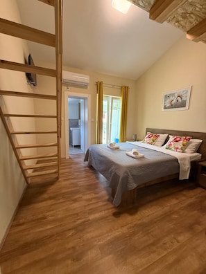 Ein Schlafzimmer mit einem Bett, einer Holzleiter, einem Badezimmer und einem Fenster mit Vorhängen.