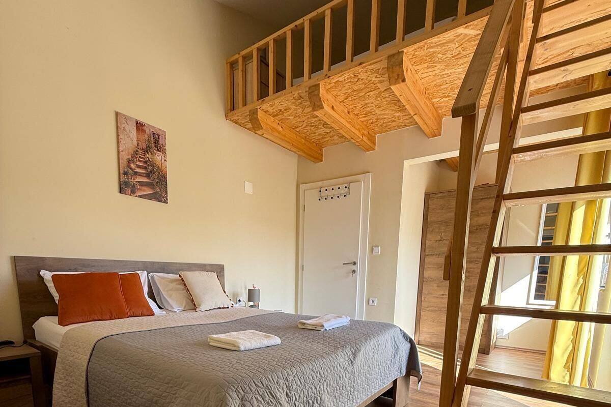 A bedroom with a wooden bed frame, a headboard, a nightstand, a bedside table, a door, and a wooden staircase.