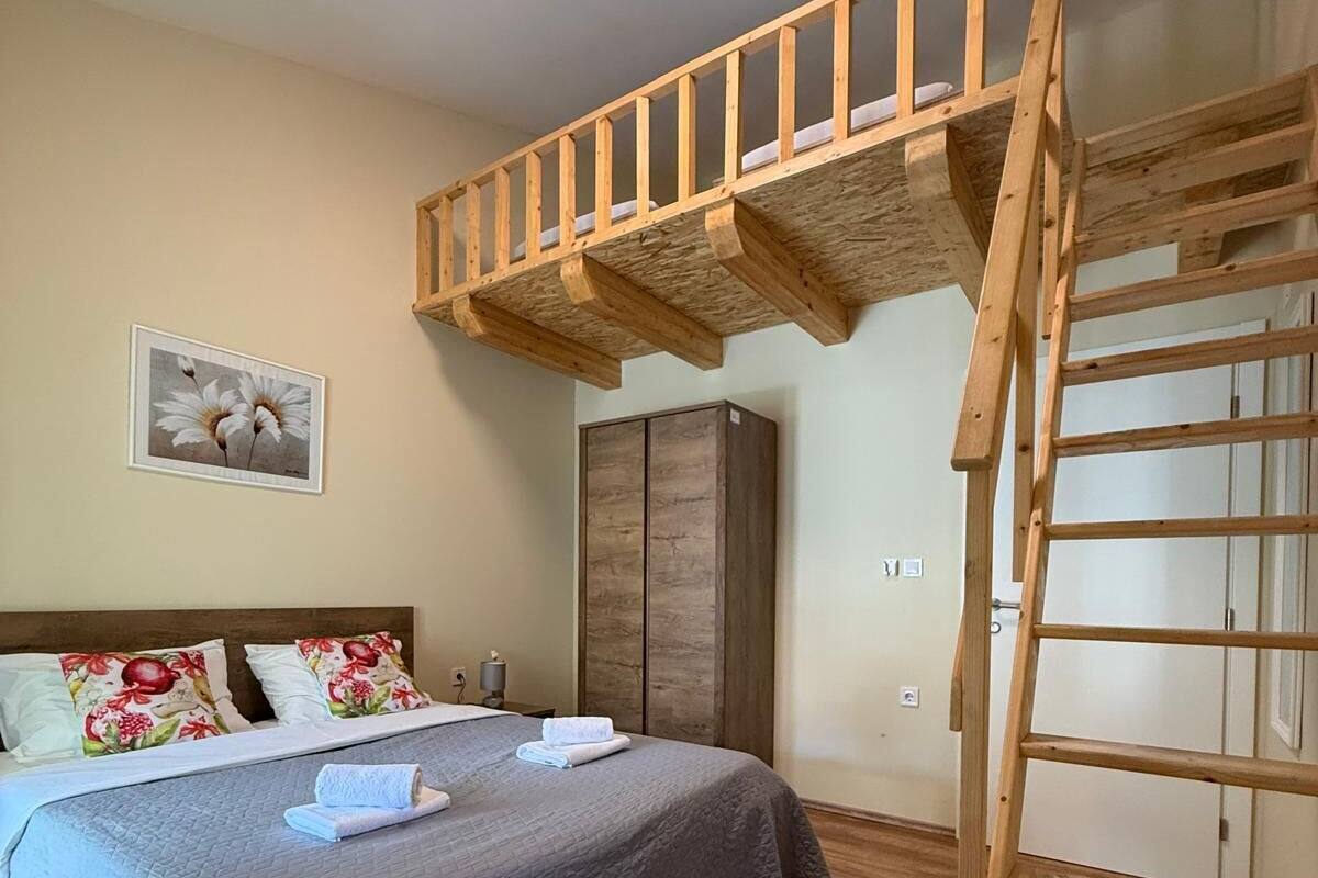 A bedroom with a bunk bed, a wooden ladder, a wardrobe, and a painting on the wall.