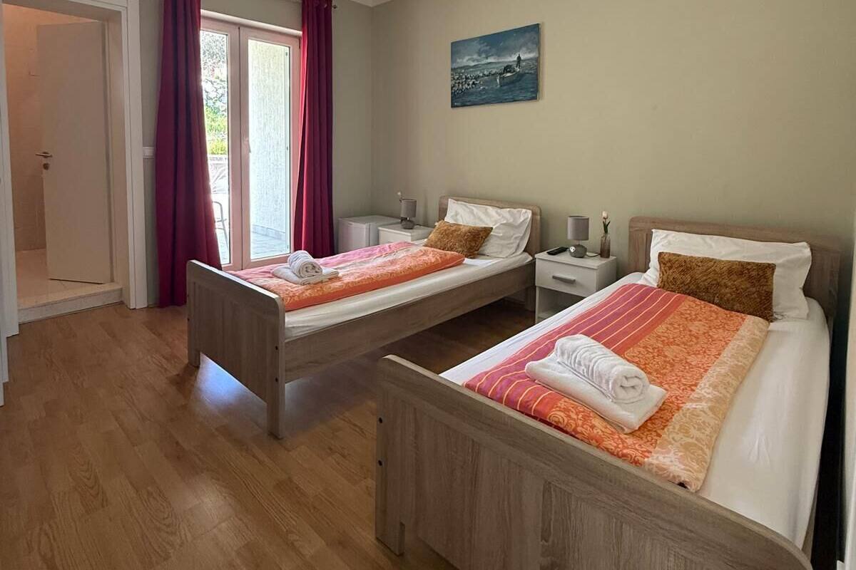 A hotel room with two wooden beds, a painting on the wall, a ceiling light, and a door leading to an outdoor area.