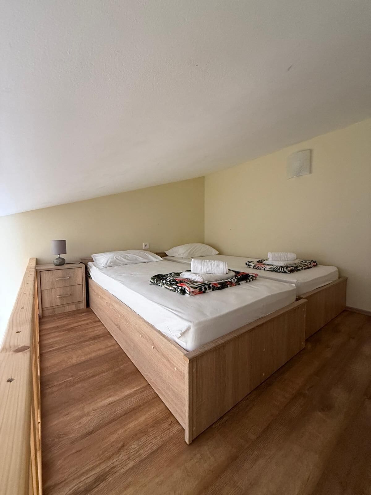 Un lit simple avec un cadre en bois, une table de chevet avec une lampe et une petite commode.