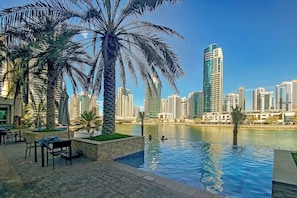 A poolside area with palm trees, a view of a city skyline, and modern buildings. - Free Housekeeping Visits During Your Stay - Stayshort - Fancy 1-bedroom Apartment Sleeps 4 in Dubai Marina (Dubai)