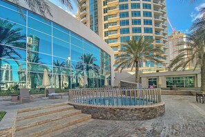 A modern building with reflective glass windows, a pool area with steps, and palm trees. - Free Housekeeping Visits During Your Stay - Stayshort - Fancy 1-bedroom Apartment Sleeps 4 in Dubai Marina (Dubai)