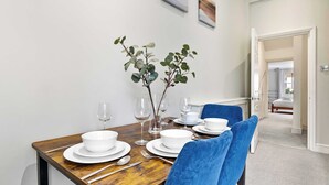 Une table à manger dressée avec des bols, des assiettes et des couverts blancs, des chaises bleues et deux vases ornés de feuillage vert.