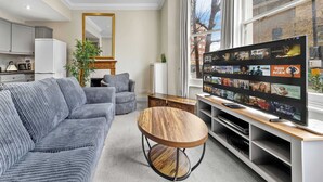 Un salon moderne avec un canapé, une table basse, un téléviseur et une fenêtre donnant sur la ville.