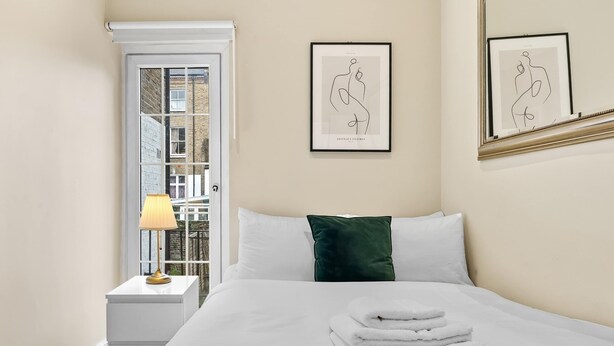 Une chambre d’hôtel avec un lit, une table de chevet, une lampe et deux œuvres d’art abstraites encadrées accrochées au mur.