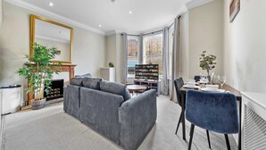 Un salon comprenant un canapé, une table à manger avec des chaises, une cheminée, une bibliothèque et un grand miroir.