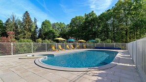 Une piscine avec une terrasse carrelée, entourée d’une clôture, et des arbres en arrière-plan.