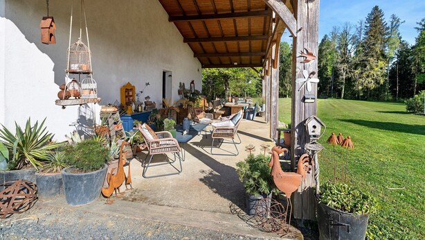 Un espace extérieur abrité, aménagé avec des meubles rustiques, des nichoirs et des plantes en pot.