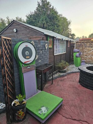 Un petit bâtiment en bois avec une porte verte, une fenêtre et un mur en briques.