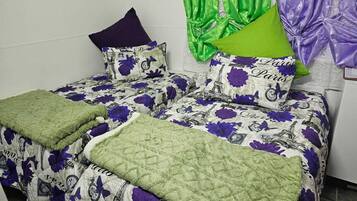 A room with two beds, each with a green quilt and purple floral bedding.