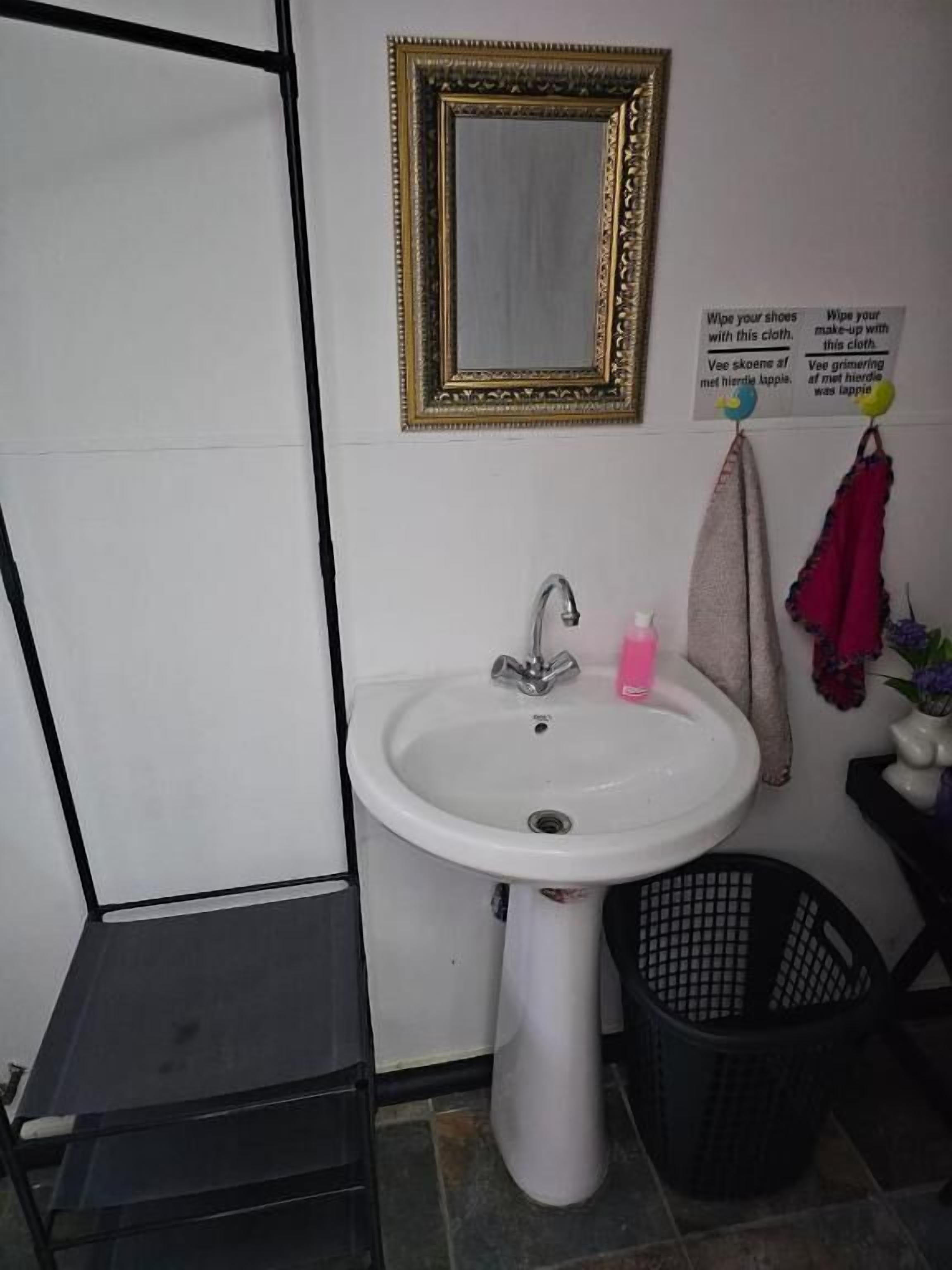 A bathroom with a white sink, a mirror with a gold frame, a black basket, and a towel rack with a pink towel.