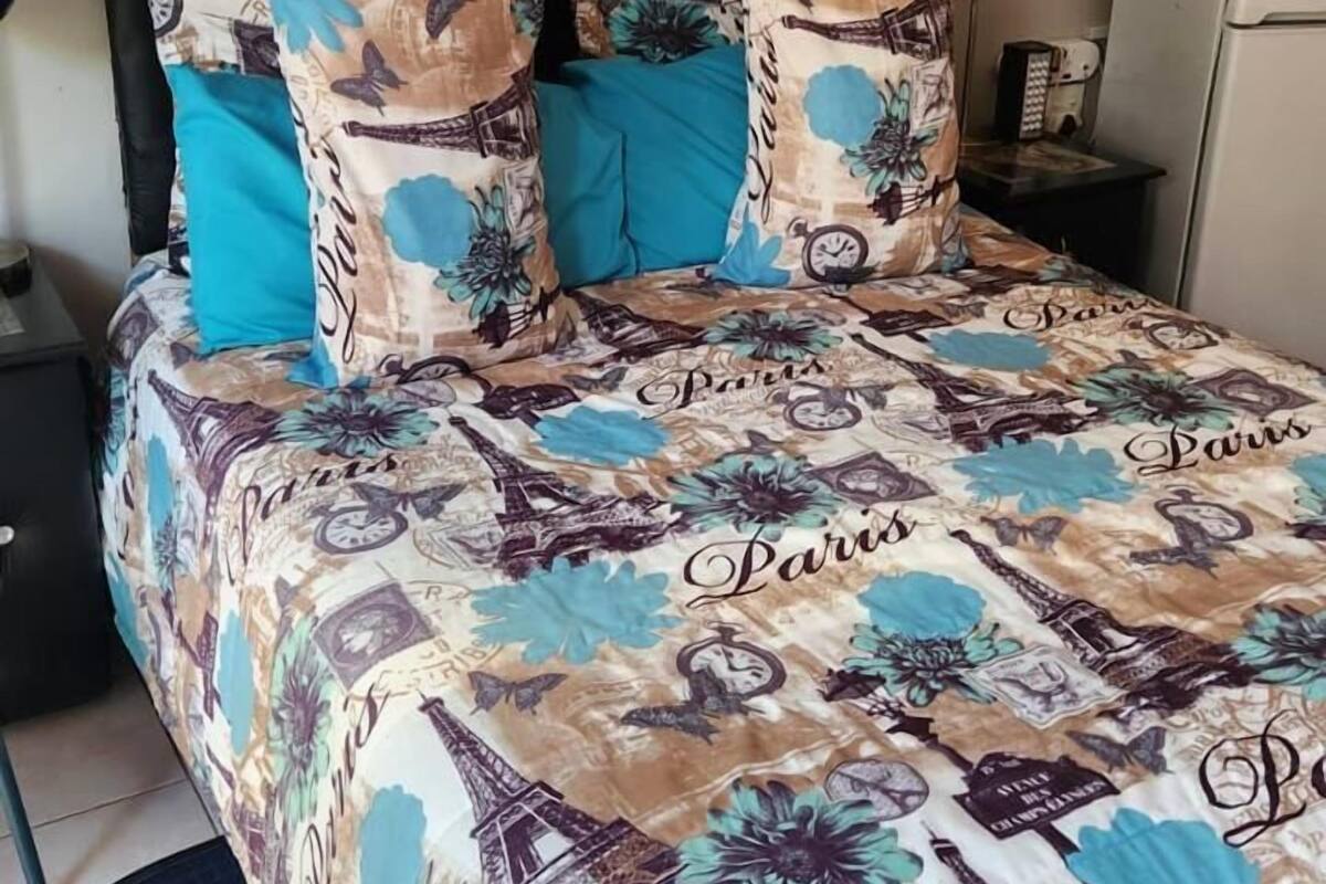 A bed with a Paris-themed bedspread, a black upholstered headboard, and a small bedside table with a lamp.