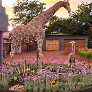 A giraffe statue in a landscaped garden with a building in the background.