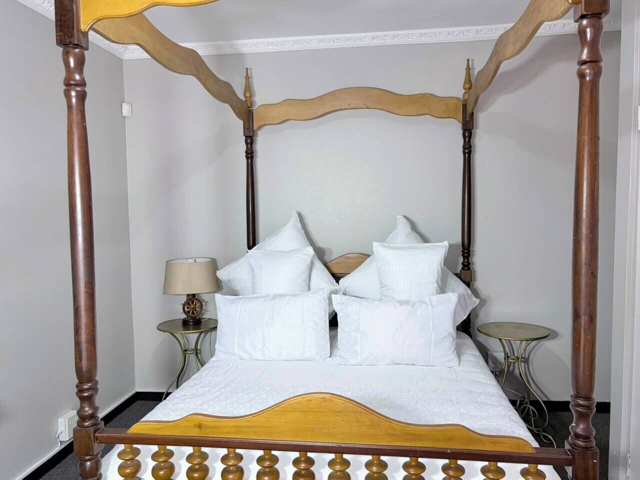 Ein Bett mit Baldachin, ausgestattet mit weißer Bettwäsche und zahlreichen Kissen, ein Nachttisch mit Lampe und ein kleiner runder Tisch.