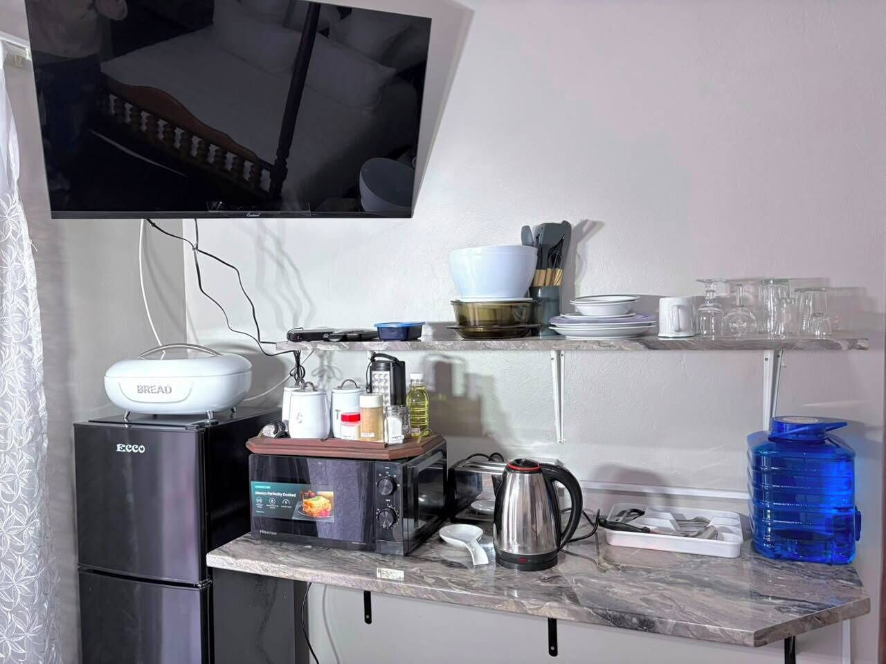A compact kitchen with a refrigerator, microwave, and a bread maker on the countertop.