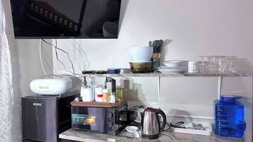 A compact kitchen with a refrigerator, microwave, and a bread maker on the countertop.