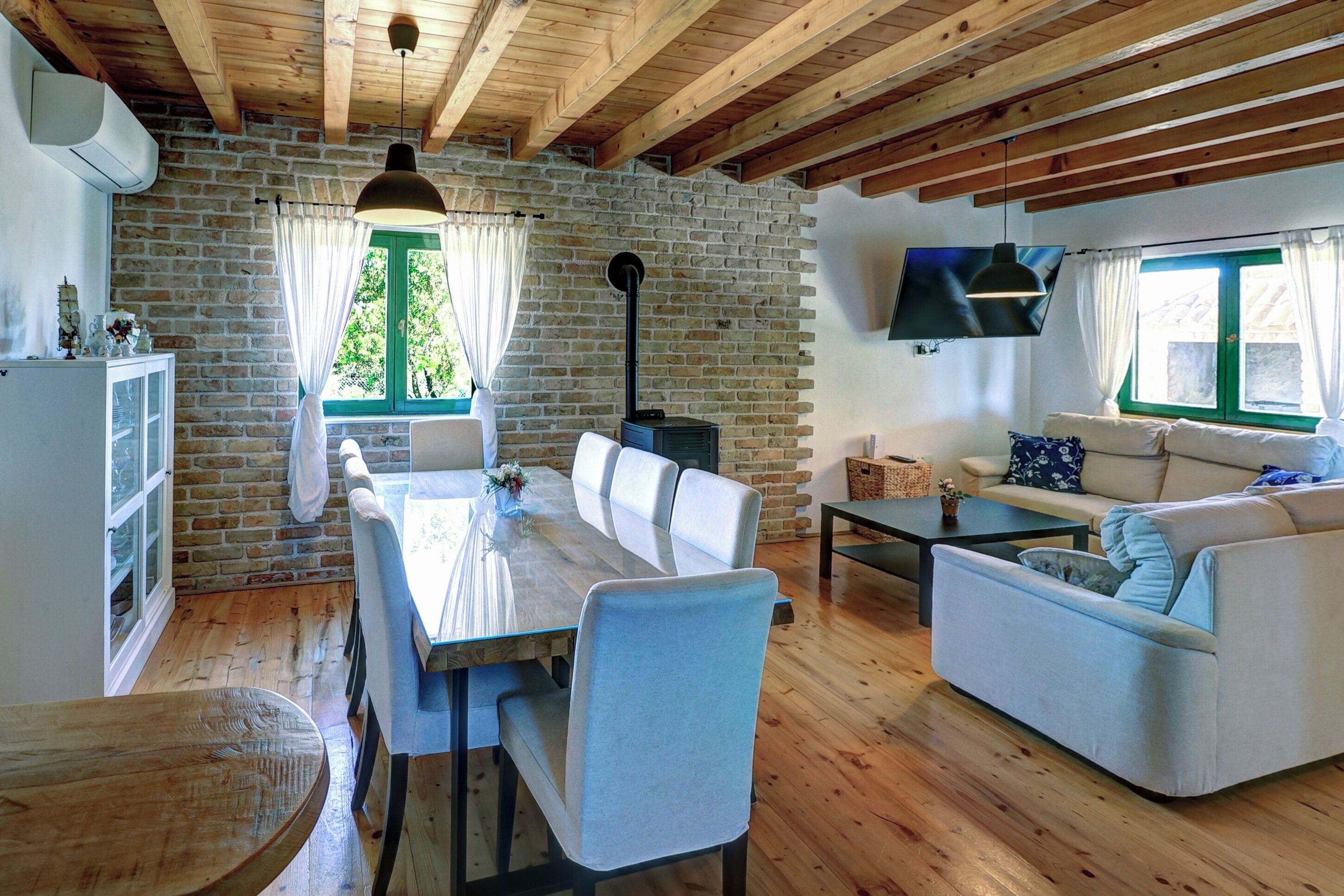 A rustic room with a dining table, chairs, a sofa, a TV, and a fireplace.