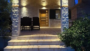 Une entrée aux murs de pierre, avec une porte en bois, deux chaises et une petite table.