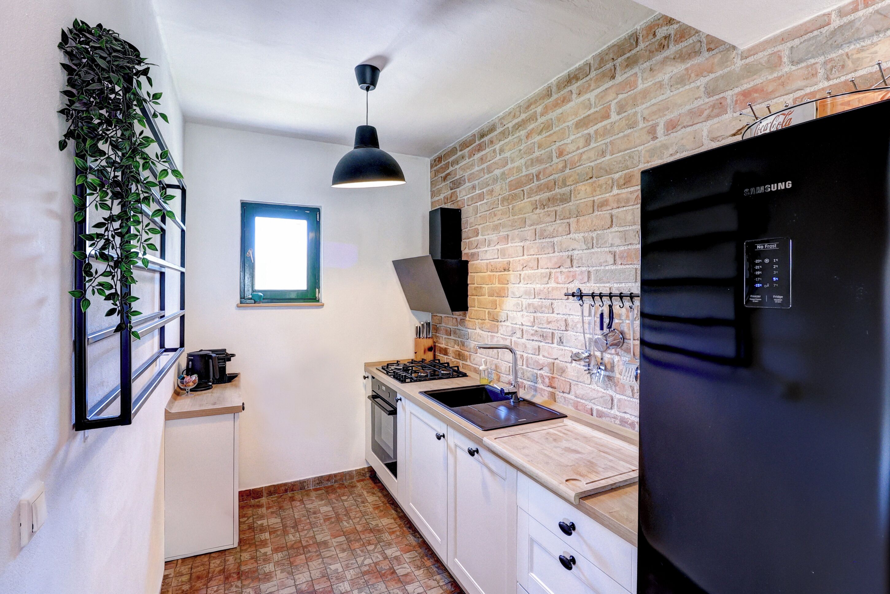 A compact kitchen with a brick wall, a black refrigerator, a sink, and a window.