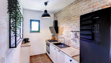 A compact kitchen with a brick wall, a black refrigerator, a sink, and a window.