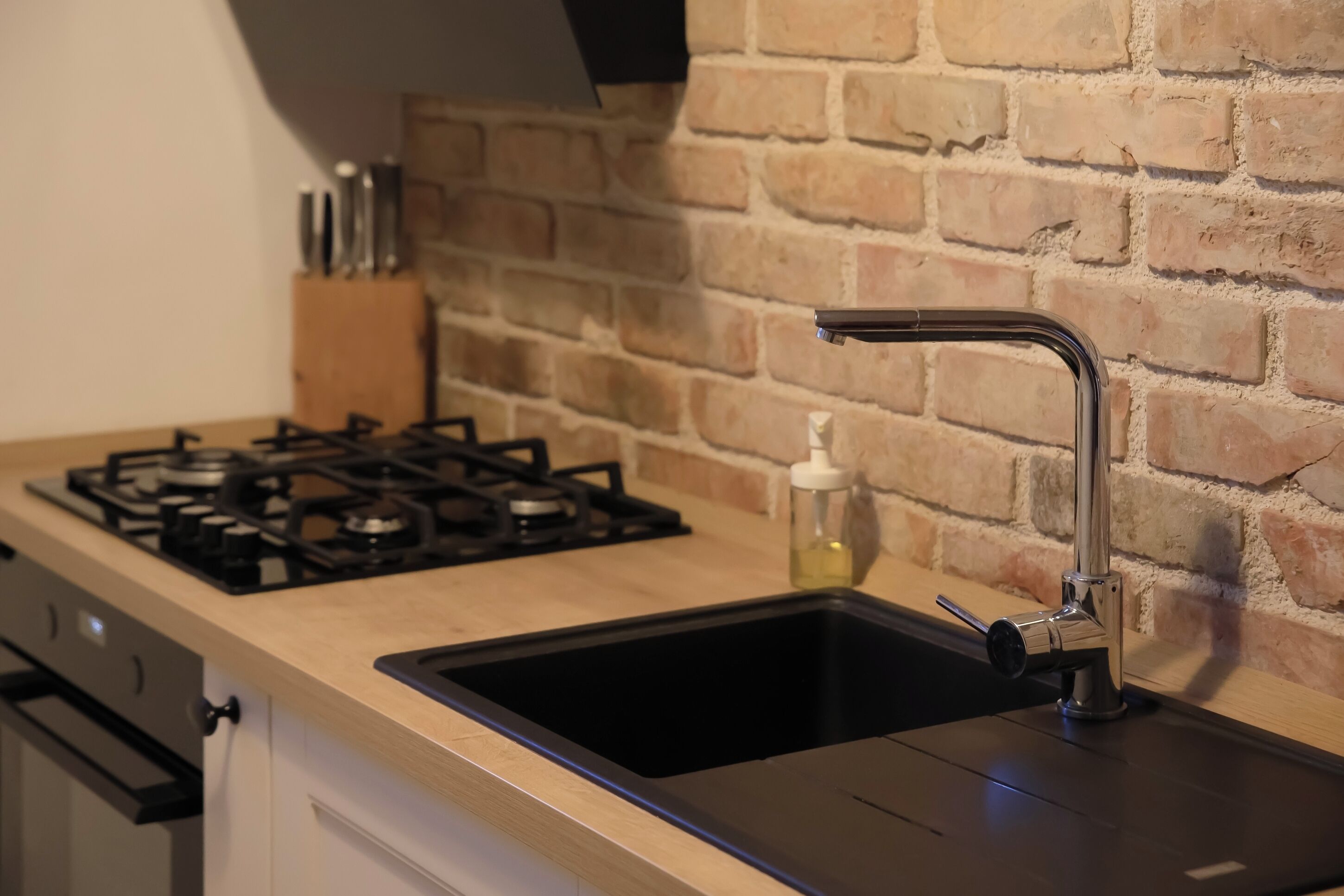 Une cuisine équipée d’une cuisinière à gaz, d’un évier et d’un mur en briques.