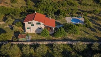 Vista aérea de una casa con techo rojo, piscina y un muro de piedra en primer plano.