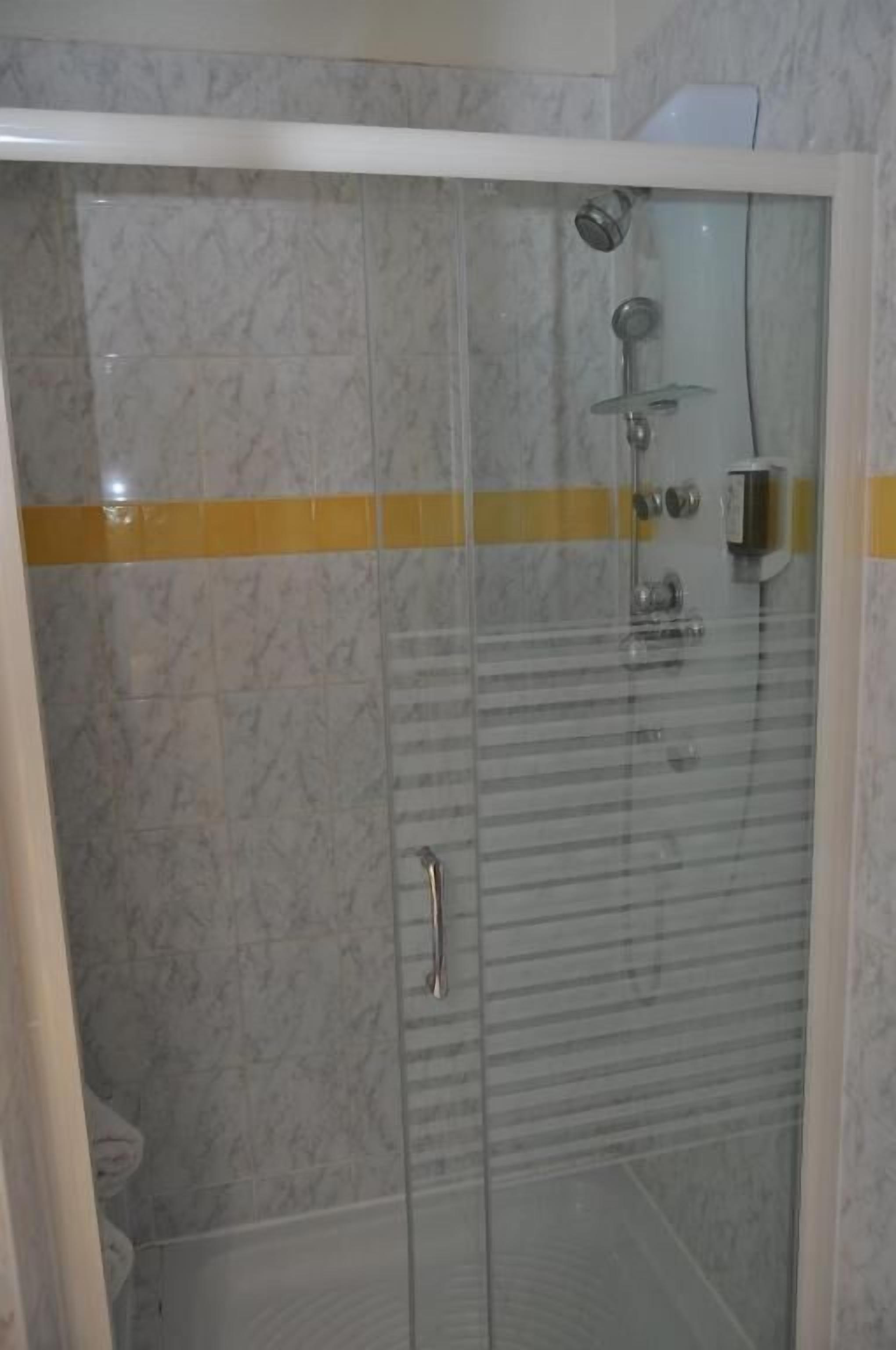 Eine Dusche mit Glasabtrennung, einer Haltestange und einem gelben Streifen an der Wand.