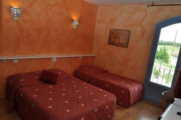 A room with two beds, a window with a view, and wall-mounted lights. - Hôtel Les Mimosas (Lunel)