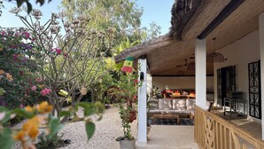 A covered outdoor seating area with a sofa and a table, surrounded by a garden with various plants and flowers. - Charming villa by the sea - Résidence Marysol (Saly)