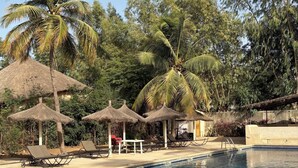 A swimming pool with lounge chairs and thatched umbrellas, surrounded by palm trees and greenery. - Charming villa by the sea - Résidence Marysol (Saly)