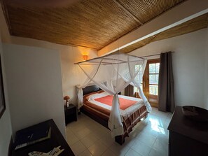 Un dormitorio con cama bajo dosel, una mesita de noche y un ventanal con cortinas.