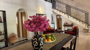 Un comedor con un jarrón de flores, un frutero y una escalera.
