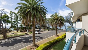 A street with palm trees, a parking lot, and a building with a balcony. - Bayview on The Esplanade (Cowes)