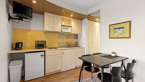 A compact kitchen with a microwave, toaster, and coffee maker on the counter, a small refrigerator, and a dining table with chairs. - Bayview on The Esplanade (Cowes)