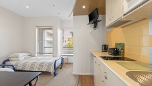 A compact room with a bed, a desk, a kitchenette, and a TV mounted on the wall. - Bayview on The Esplanade (Cowes)