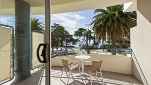 A balcony with a table and chairs, overlooking a scenic view with palm trees and a body of water. - Bayview on The Esplanade (Cowes)