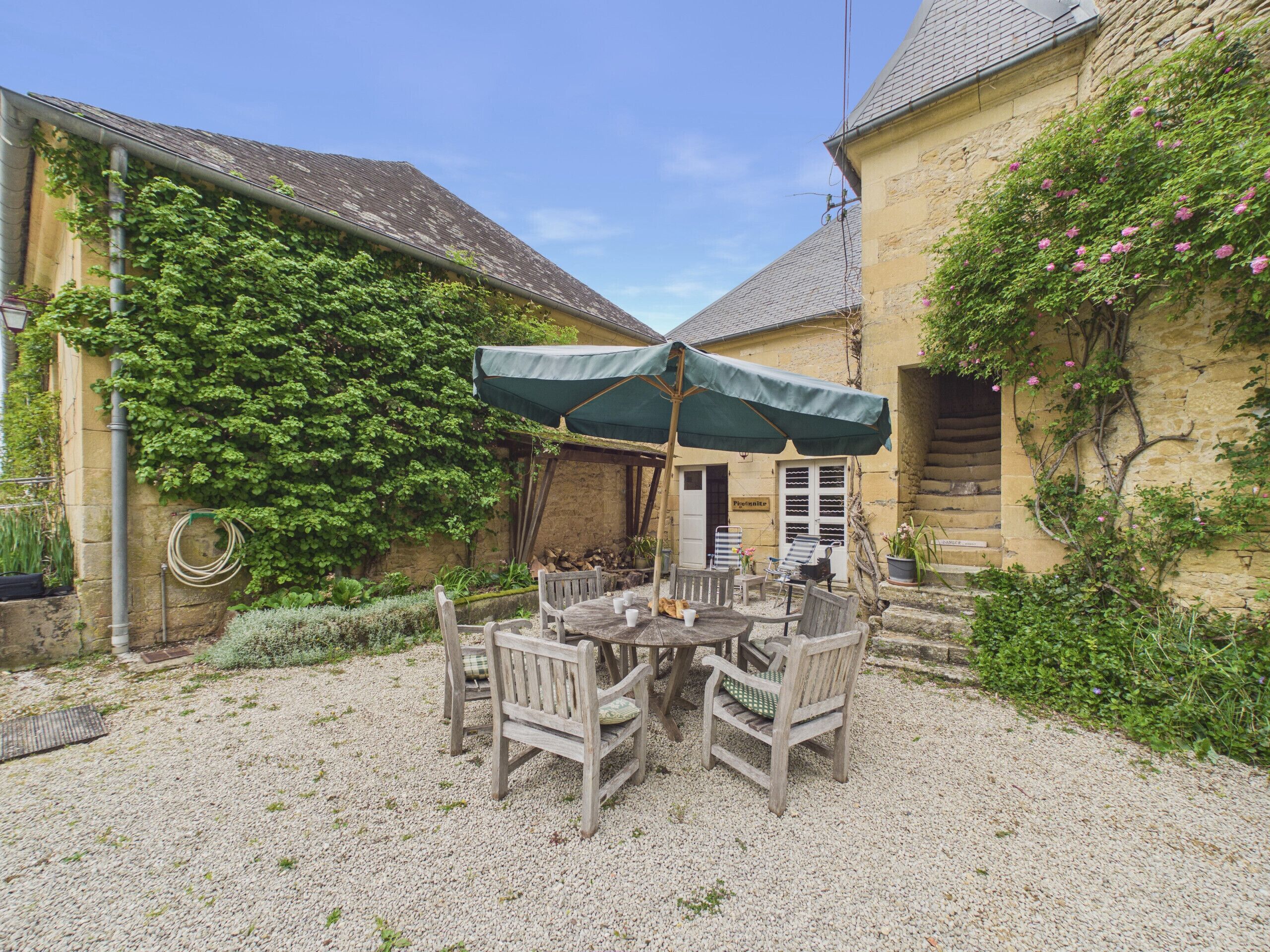 A courtyard with a round table and chairs, a green umbrella, and a stone wall with climbing plants.