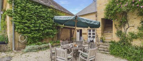 A courtyard with a round table and chairs, a green umbrella, and a stone wall with climbing plants.