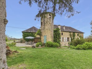 A stone tower, a stone building with a pitched roof, and a grassy yard with outdoor furniture.