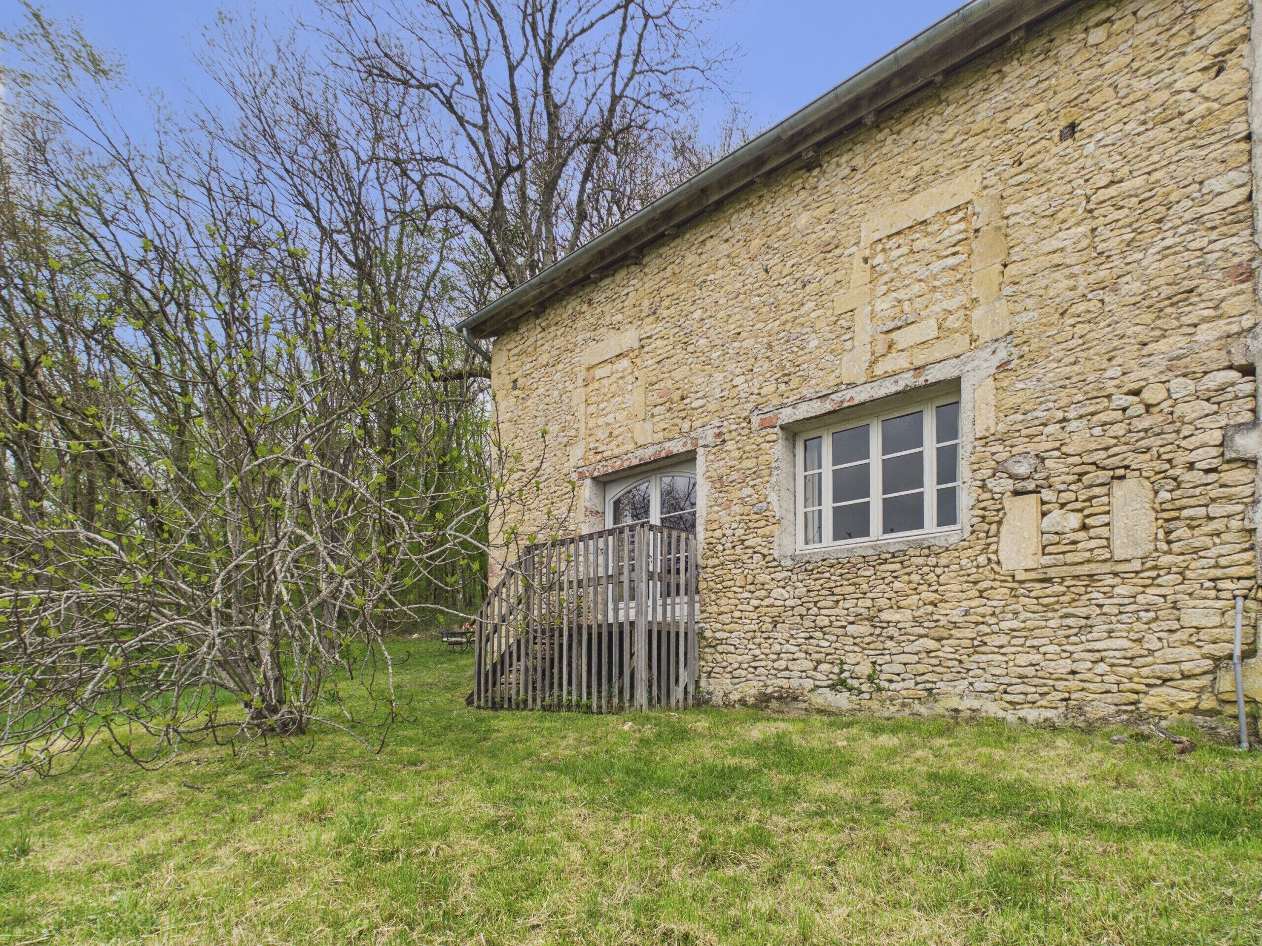 A stone building with a wooden gate, a window, and a tree in the foreground.