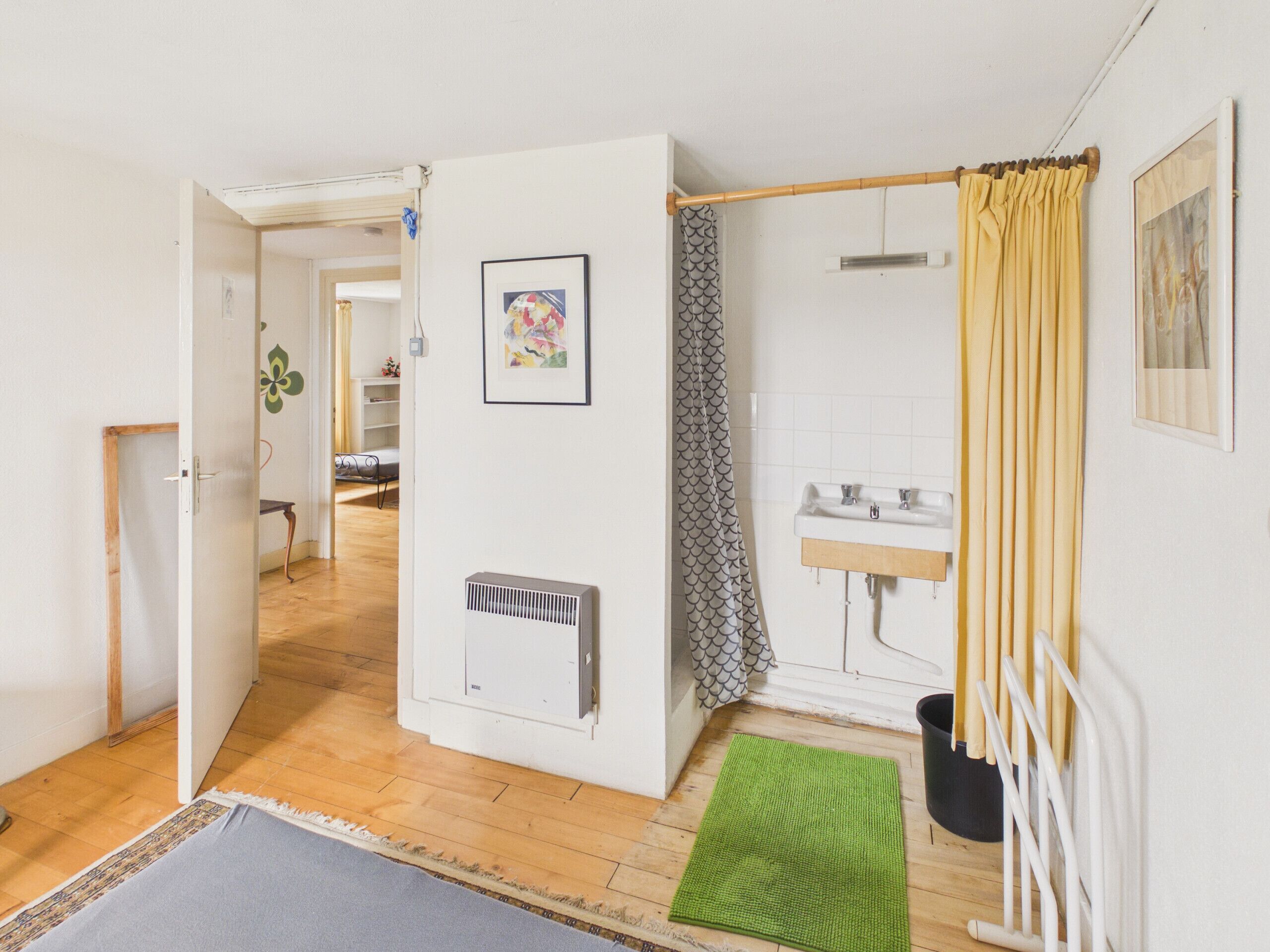 Una habitación con cama, baño con cortina de ducha, radiador y alfombra verde.