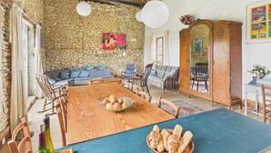 Een eetgedeelte met een houten tafel, stoelen, een schaal fruit en een fles wijn.