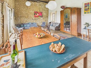 A dining area with a wooden table, chairs, a bowl of fruit, and a bottle of wine. - Large 11-guest cottage, shared pool & nature (Fanlac)
