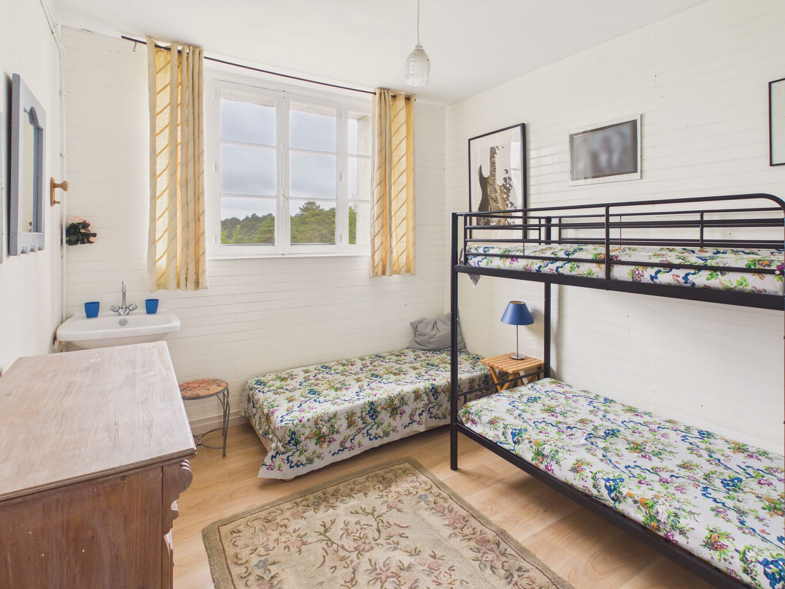 A dormitory room with bunk beds, a sink, a small table, and a window with curtains.