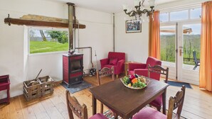A cozy room with a wooden table, red chairs, a red stove, and a large window with a view of greenery. - La Sonnerie, nature cottage & shared pool (Fanlac)