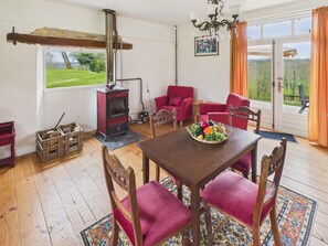 A cozy room with a wooden table, red chairs, a red stove, and a large window with a view of greenery. - La Sonnerie, nature cottage & shared pool (Fanlac)