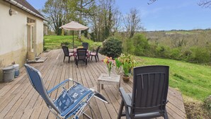 A wooden deck with a table and chairs, a potted plant, and a view of the countryside. - La Sonnerie, nature cottage & shared pool (Fanlac)