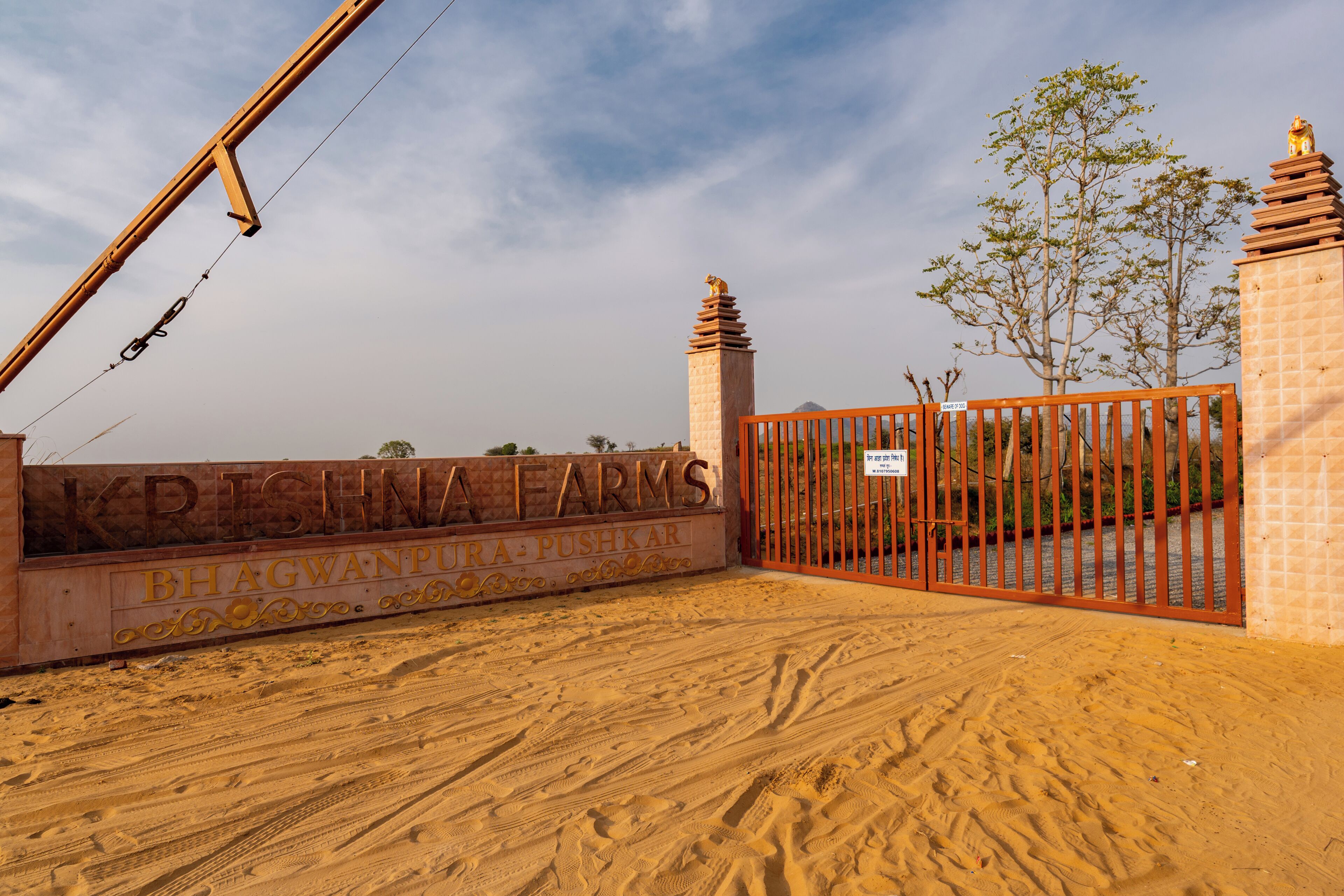 Uma entrada com portão e placa com as inscrições 'KRISHNA FARMS' e 'BHAGWANPURAPUSHKAR'.